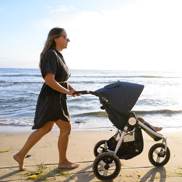 Bumbleride Indie on beach with family walking with surfboard