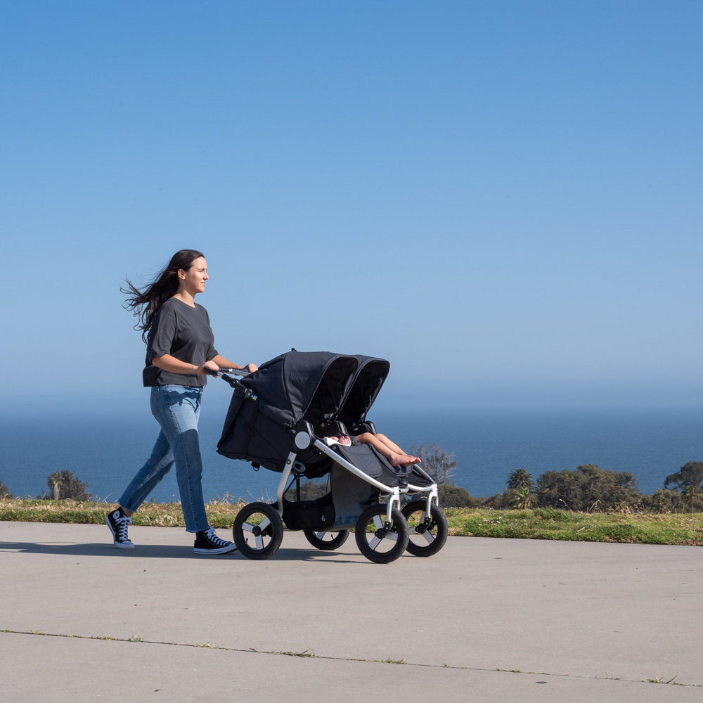 
                      
                        Picture of mother pushing Bumbleride Indie Twin double stroller in dusk on concrete in front of ocean and trees in background. Global
                      
                    