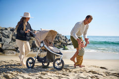 Father holding sons arms on sand at beach with mother walking next to them pushing Bumbleride Indie all terrain stroller in Sand. - New Collection 2022 - Global