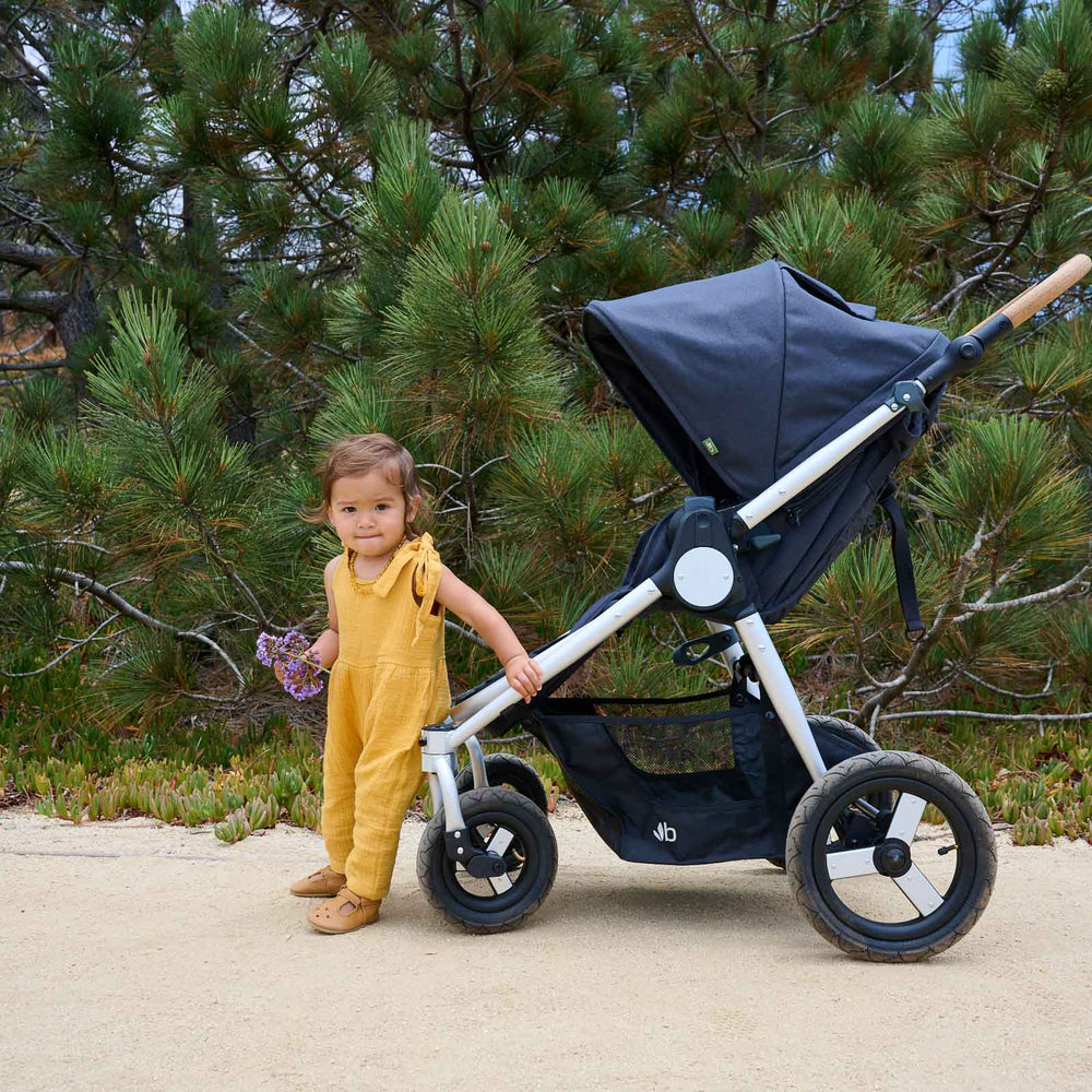 
                  
                    Picture of toddler baby holding purple flowers standing in front of Bumbleride Era reversible stroller in Dusk on dirt trail. New Collection 2022 - Global
                  
                