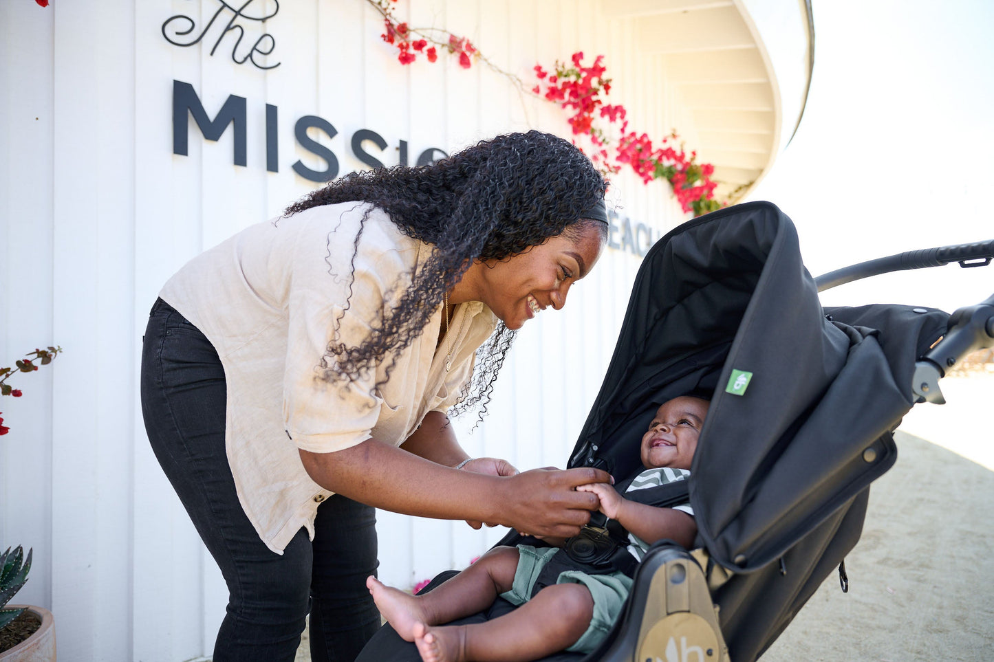 Mother leaning towards stroller seat with smiling baby sitting in bumbleride indie all terrain stroller in black - New Collection 2022 - Global