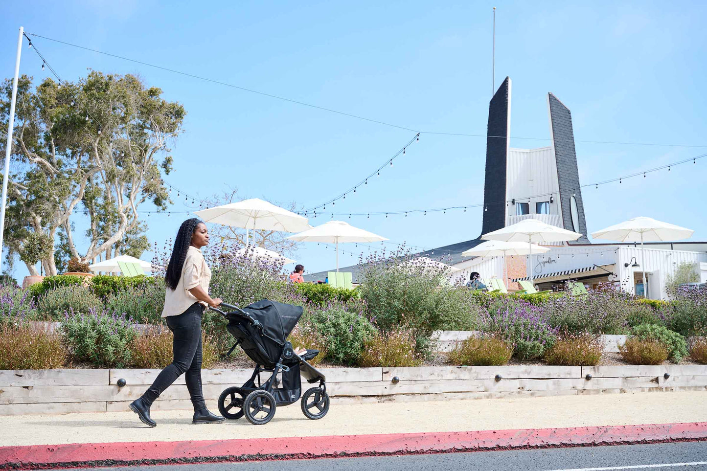 Mother pushing Bumbleride Indie in Matte Black in front of flowers on sidewalk in front of store in background - New Collection 2022 - Global