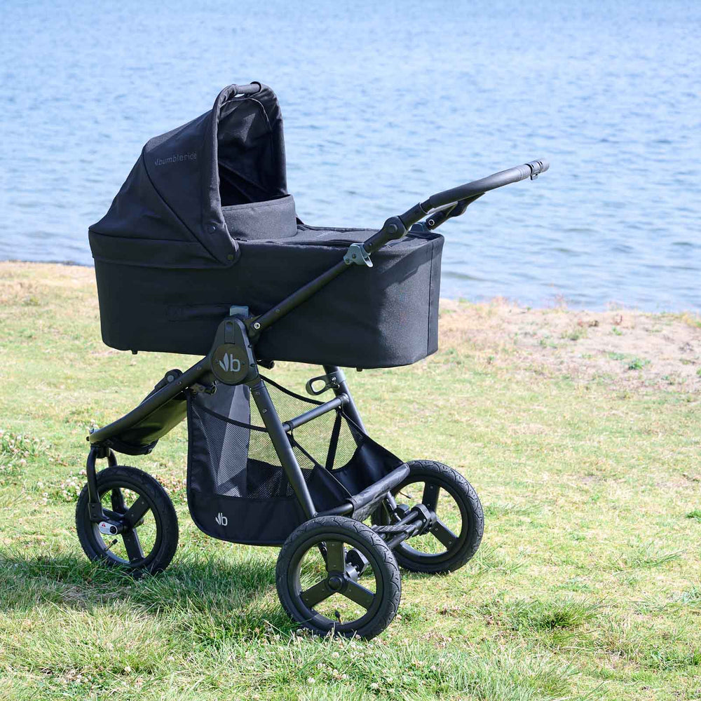 
                  
                    Bumbleride Single Bassinet in Black attached on Bumbleride Indie All Terrain Stroller in Black on grass near water . Global
                  
                