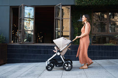 Mother pushing Bumbleride Era reversible stroller in Sand on sidewalk in front of restaurant. New Collection 2022. Global