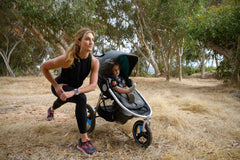 Mother stretching next to IRONMAN stroller by Bumbleride with her toddler looking into the distance.