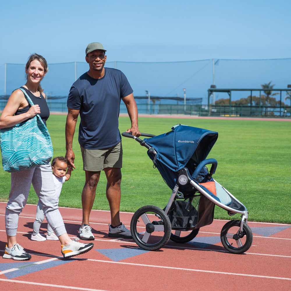 
                  
                    Bumbleride Tote being held by mother walking with child and husband while holding hands on a running track
                  
                
