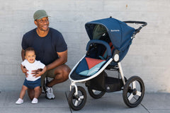 Picture of smiling father kneeling while holding smiling toddler next to Bumbleride Speed jogging stroller in Supernova. New Collection 2022. Global