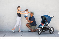 Picture of mother and father playing with toddler in the air while next to Bumbleride Speed jogging stroller in Supernova. Global