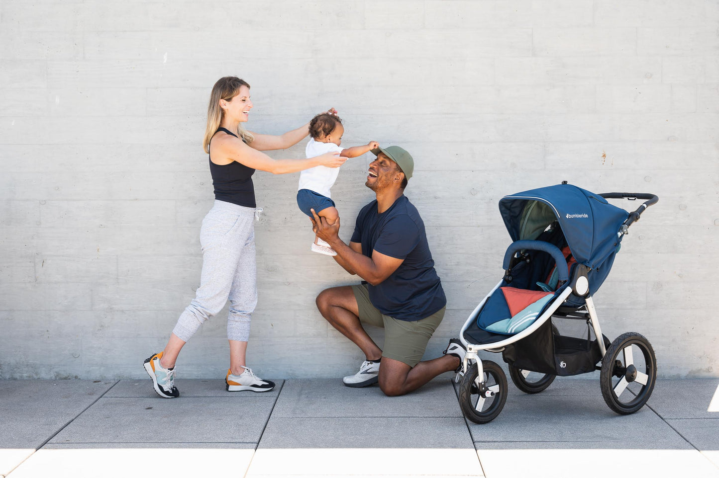 Picture of mother and father playing with toddler in the air while next to Bumbleride Speed jogging stroller in Supernova. Global
