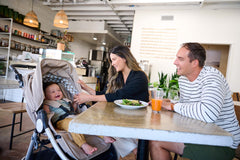 Mother and Father sitting at table with child sitting in Era reversible stroller in Sand - New Collection 2022 - Global