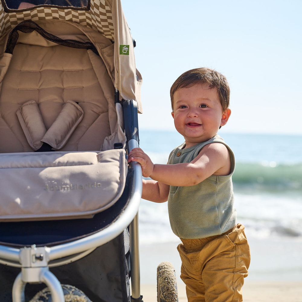 
                  
                    Picture of baby boy holding onto Indie All Terrain stroller frame while at the beach with ocean in background. New Collection 2022 - Global.
                  
                